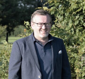 Bürgermeister Christian Schlegel steht vor einen Hecke und sieht lächelnd in die Kamera